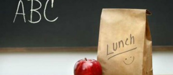 Bolsa de lunch escolar con una manzana a un lado y un pizarrón de fondo con las letras ABC