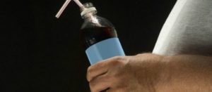 Acercamiento al abdomen de perfil de una persona con una botella de bebida azucarada en la mano