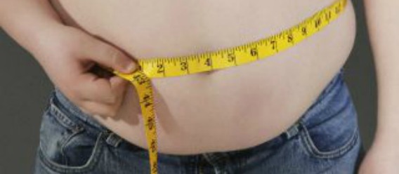 Adolescente con sobrepeso midiéndose la barriga con una cinta métrica