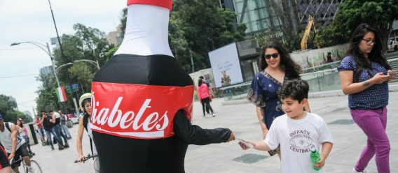 Botarga de refresco de Cola con la leyenda Diabetes entregando volantes informativos a personas que pasan por la calle