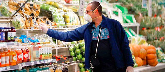 Hombre con tapabocas seleccionando verduras en en refrigerador de súper