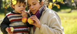 Madre mostrando manzanas a su hijo al pie de un manzano
