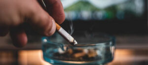 Mano de fumador tirando la ceniza de su cigarrillo en un cenicero